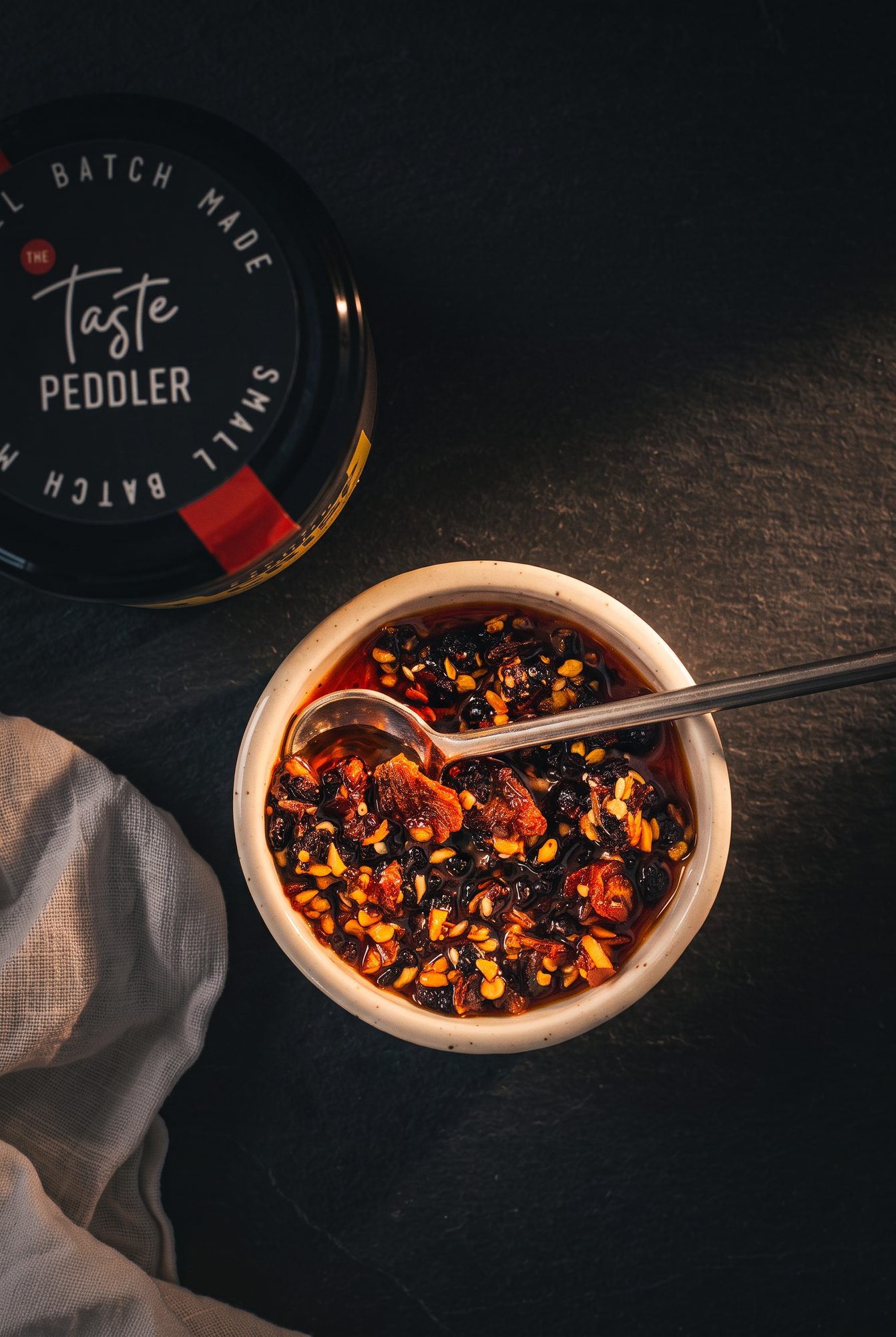 Overhead bowl of chilli crisp with a spoon beside the jar lid