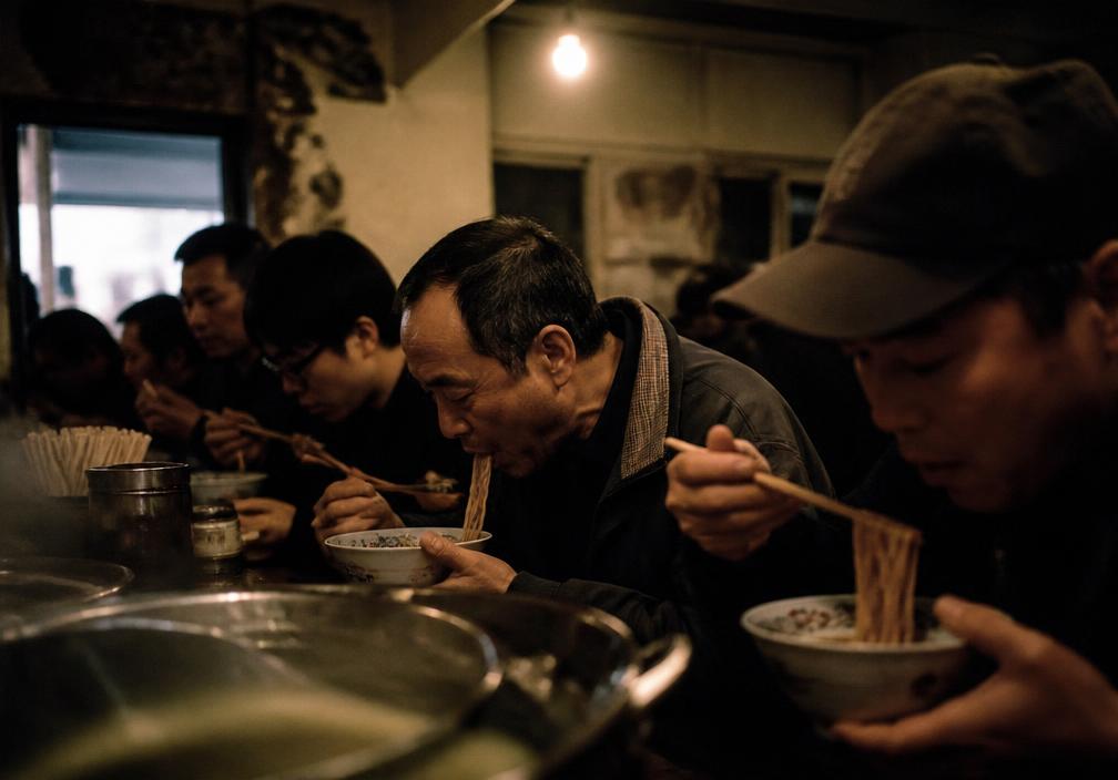 Diners eating noodles shoulder to shoulder at a small Taiwanese noodle shop in Hsinchu